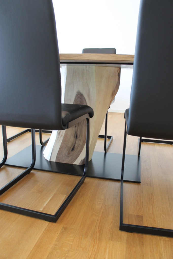 Tischbein eines massiven Nussbau-Holz-Tisch versteckt hinter Stühlen